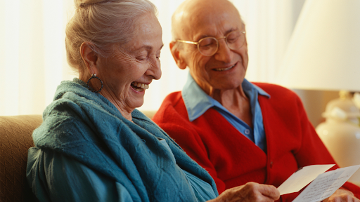 An elderly couple smiling and looking at cards.